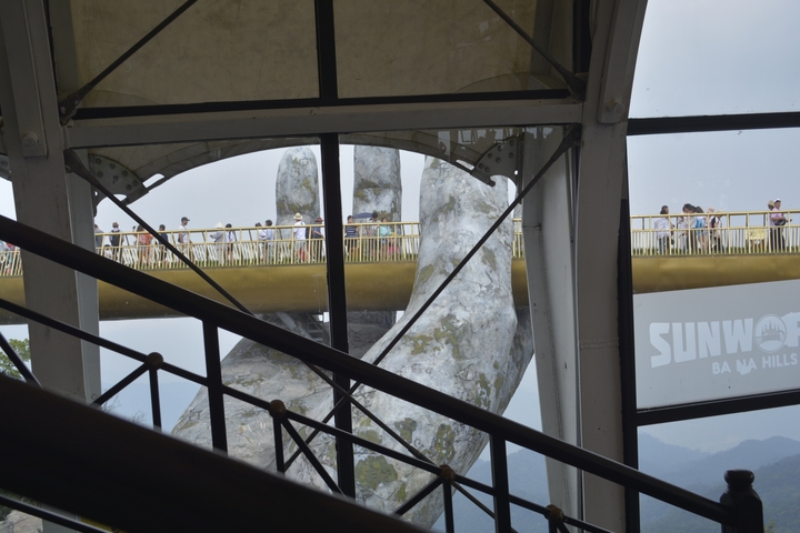 Tourists walk across the Golden Bridge supported by giant hands.