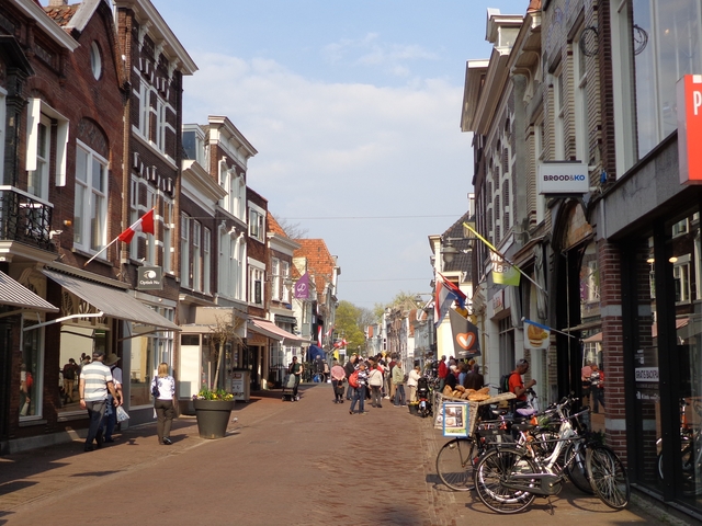 Bustling street in a Dutch city with shops and flags.