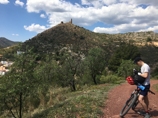       Person with a bike on a trail with ruins on a hill.
  