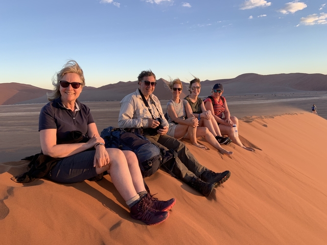       Group of people seated on a sand dune.
  