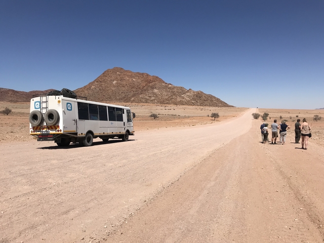       Group of people walking near a tour bus on a gravel road.
  