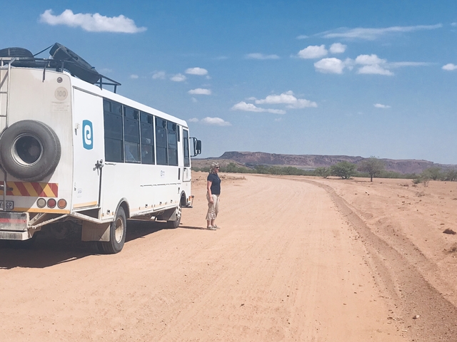 A person standing beside a tour bus on a dirt road.