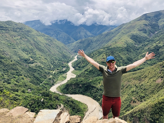 Person with arms raised in front of a valley with a river.