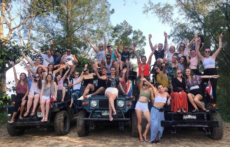 Large group of people posing on jeeps in a forest setting.