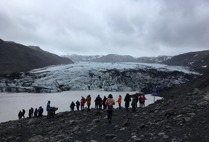       People trekking towards a large glacier.
  