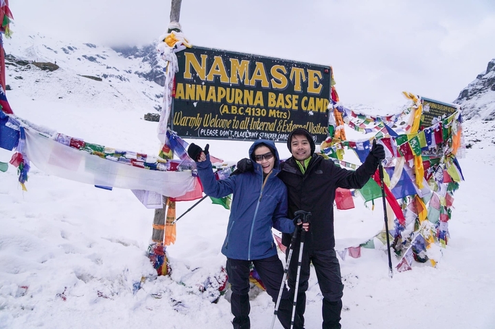       Two people at Annapurna Base Camp with snow and prayer flags.
  