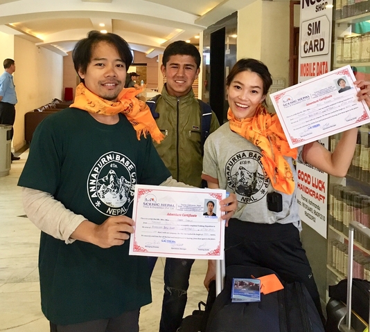       Three people holding certificates indoors, wearing orange scarves.
  