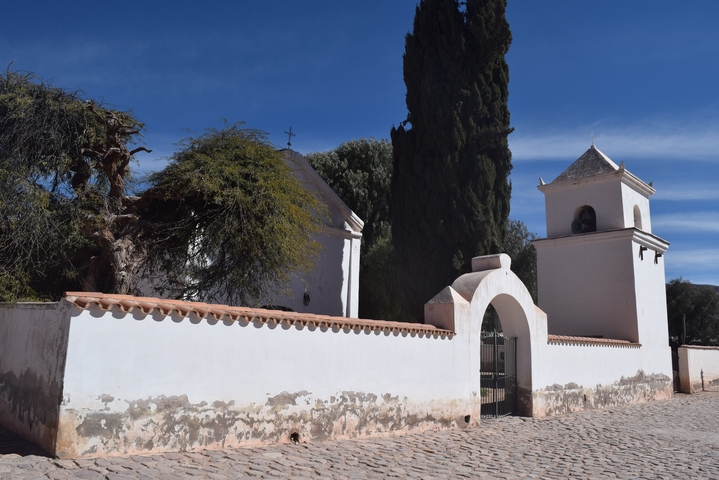Simple white structures with a bell tower and trees.