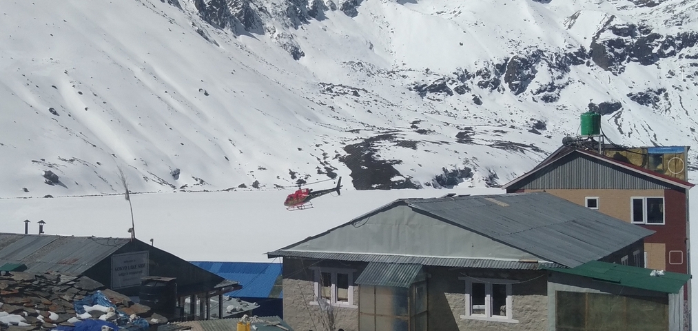 Helicopter flying over a snow-covered village with mountains in the background.