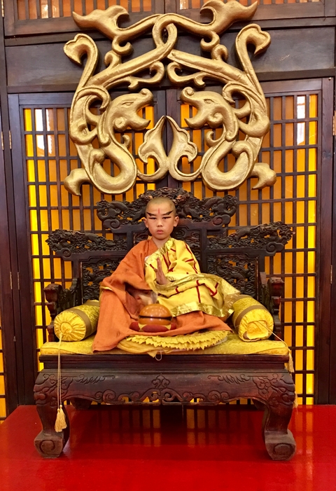 Child dressed as a monk sitting on a throne.