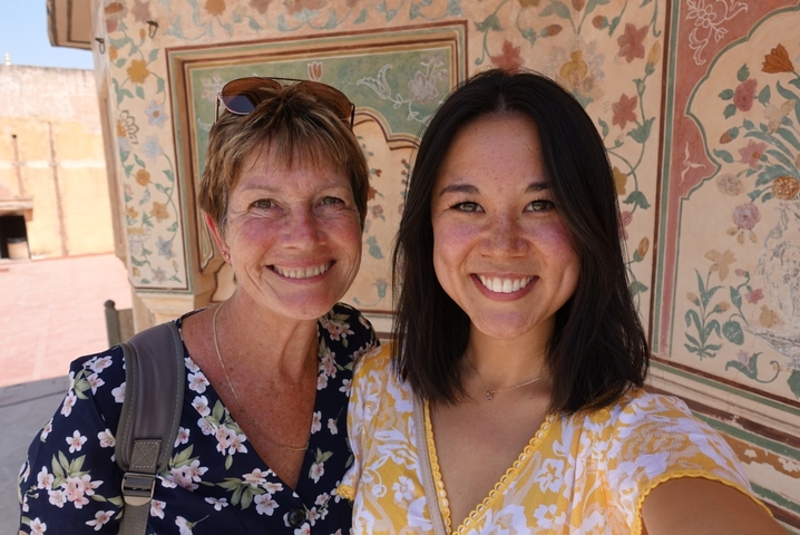 Two women smiling in front of a decorative wall.