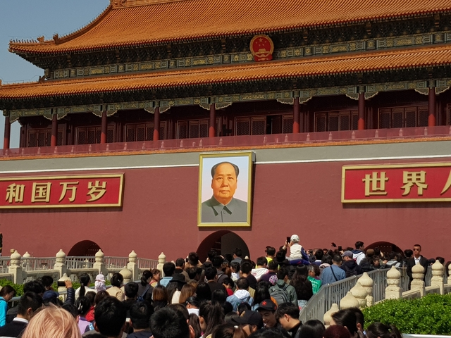 Entrance to a historic site with large portrait and crowds of people.
