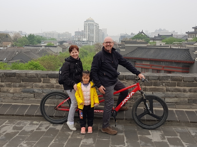 Family on a bicycle on top of a city wall with a cityscape in the background.