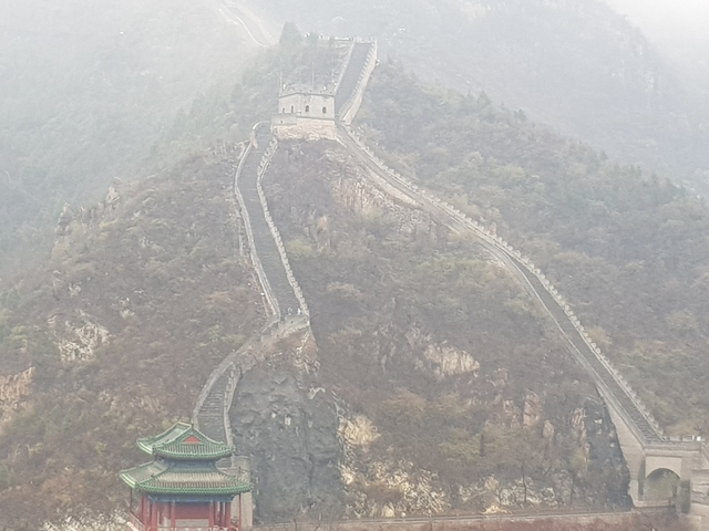 Hazy view of the Great Wall of China extending through mountainous terrain.