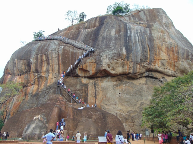 People climbing the stairs of a large rock formation.