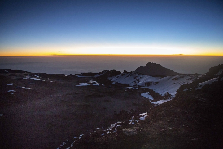       Sunrise over a mountainous landscape with snow patches.
  