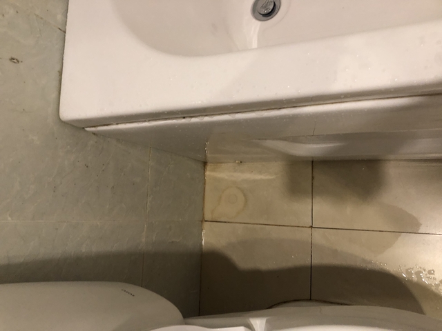 Sink pedestal corner with floor tiles showing water stains.