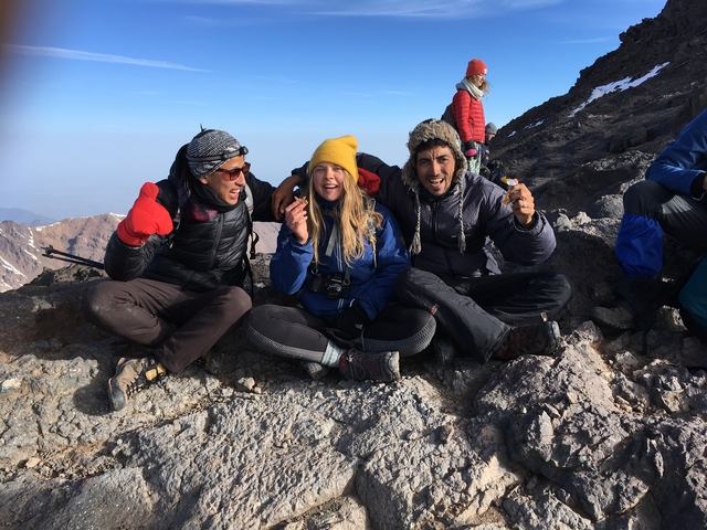 Group photo of people seated on rocky terrain near a mountain.
