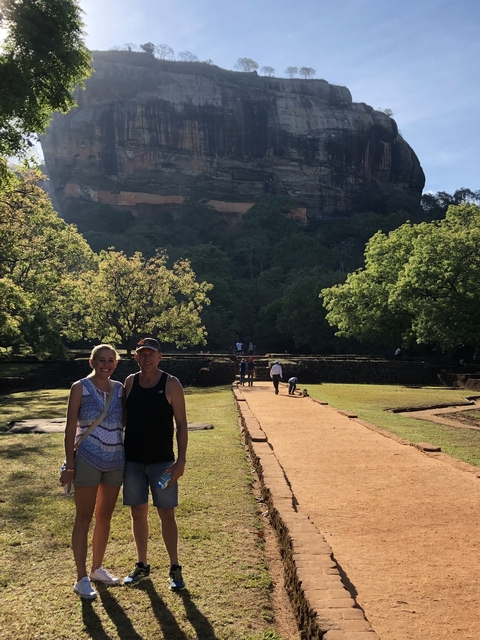 Couple posing in front of a historical site with lush trees.