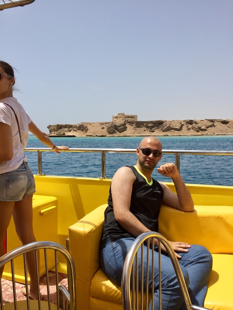 A man sitting on a boat with a coastal view in the background.