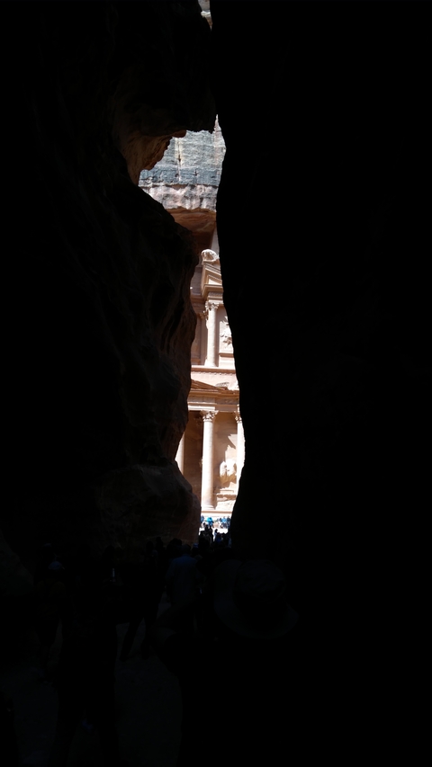 Peek through a narrow rock fissure at an ancient architectural structure.