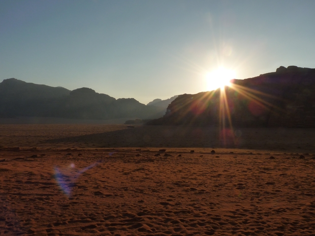 Desert landscape with sun setting behind mountains.