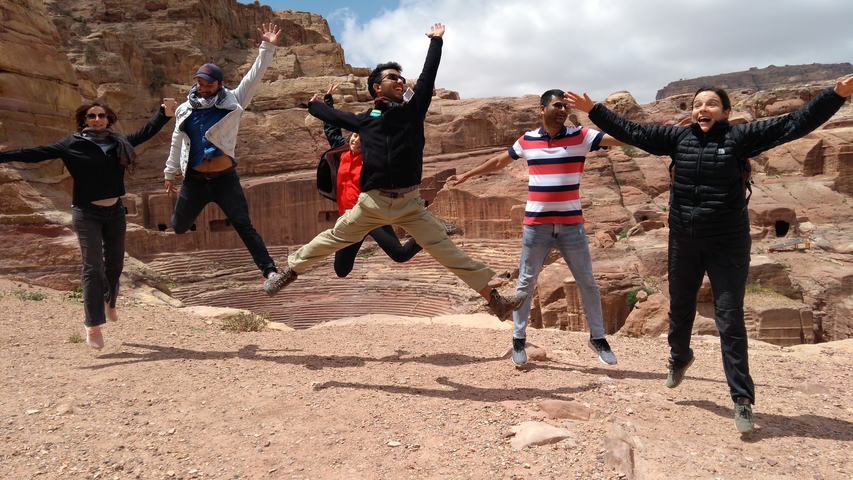 Group of tourists jumping with ancient rock formations in the background.