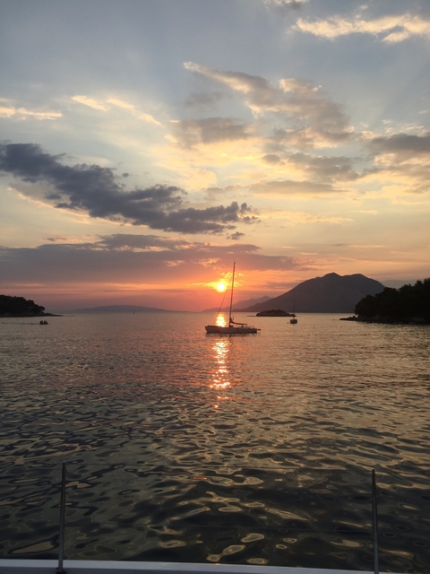       Sunset over the sea with sailboats silhouetted.
  