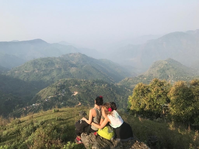       Two people sitting on a hill overlooking a lush valley.
  