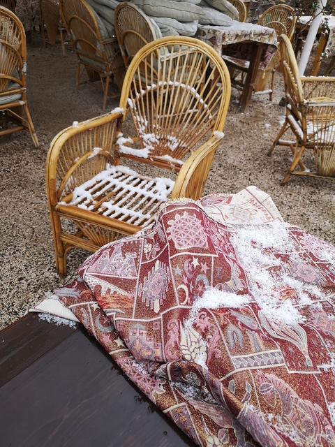       Rattan chairs covered with snow and a traditional patterned rug.
  