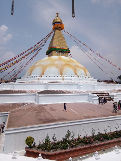 Large stupa with prayer flags and people walking around.