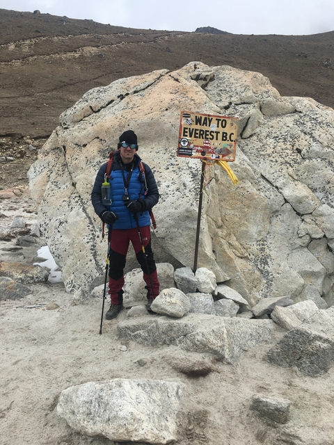       Trekker standing at Everest Base Camp sign with hiking poles
  