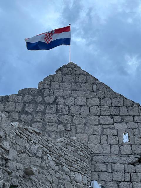       Croatian flag flying on top of a stone structure.
  