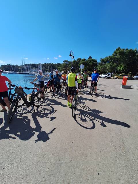       A group of cyclists near a marina with boats and clear skies.
  