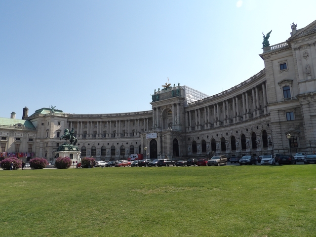       A grand, semi-circular building with equestrian statue and parked cars.
  