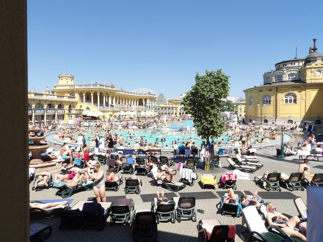A large outdoor thermal pool with many visitors, surrounded by historic architecture.