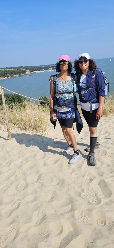       Two people posing on sand dunes with a view of the water.
  