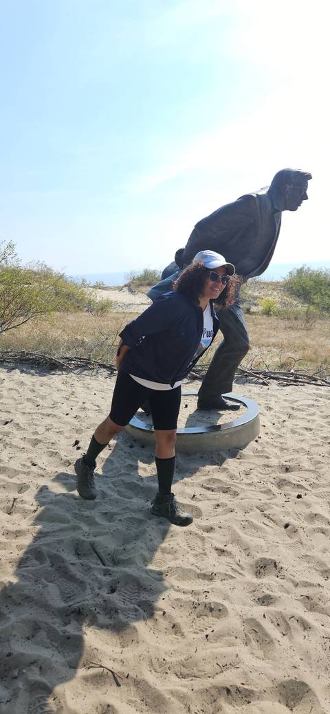      Person posing with a statue on sand.
  
