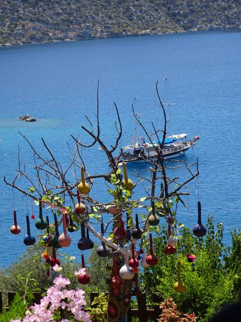       Brightly colored ornaments hanging from a tree with a sea and boat view.
  