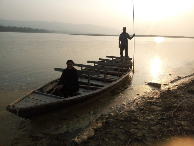 Silhouetted figures on a boat at sunset on a riverbank.