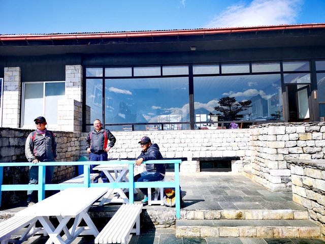      People standing outside a stone building with a mountain reflection in the window.
  