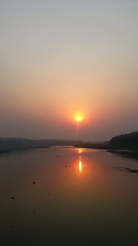 Sunset over a calm river surrounded by trees.