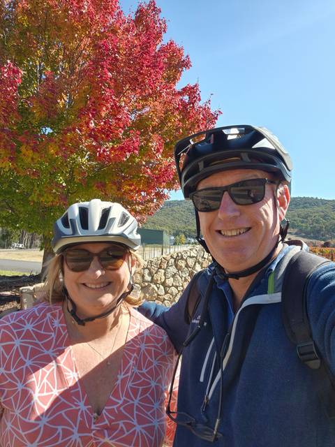 Two people wearing helmets near a colorful tree.