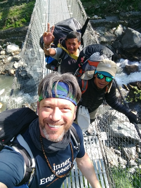       People smiling on a hanging bridge over a river.
  