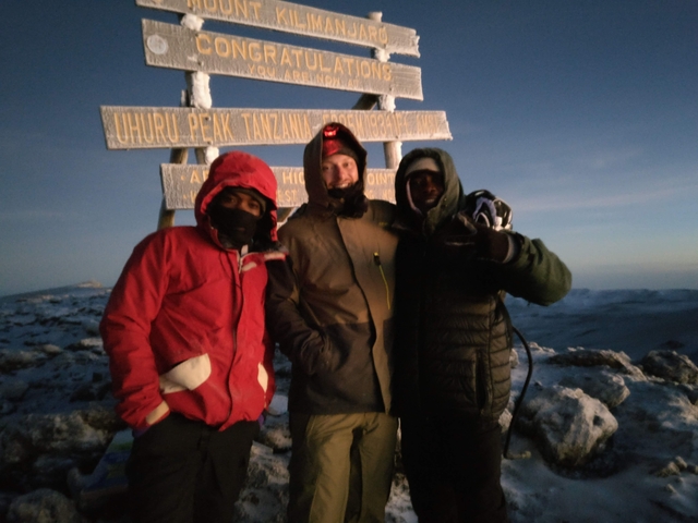 Three people posing at the top of Mount Kilimanjaro at night.