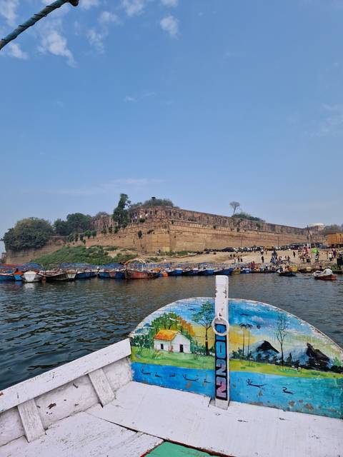 Colorful boat docked on a river with a rocky hillside in the background.