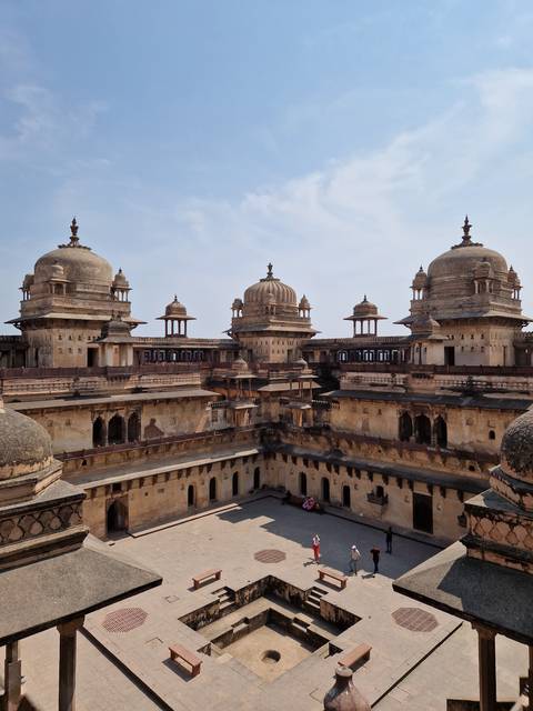       Orchha palace with tourists walking around its courtyards.
  