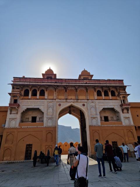       Sunshine over a grand fort entrance with tourists exploring.
  
