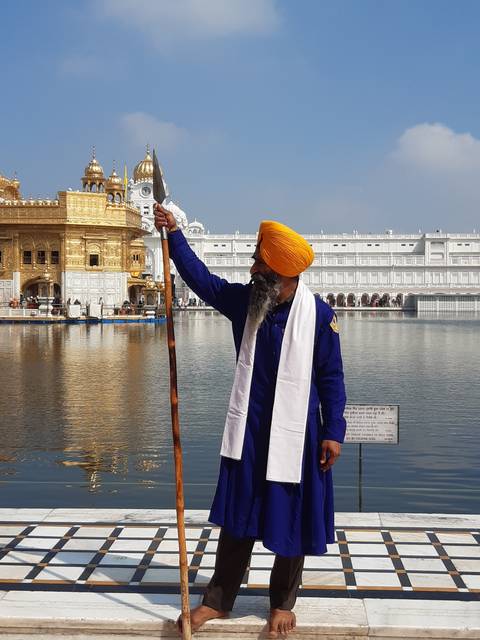 A person in traditional attire standing by water with a building in the background.