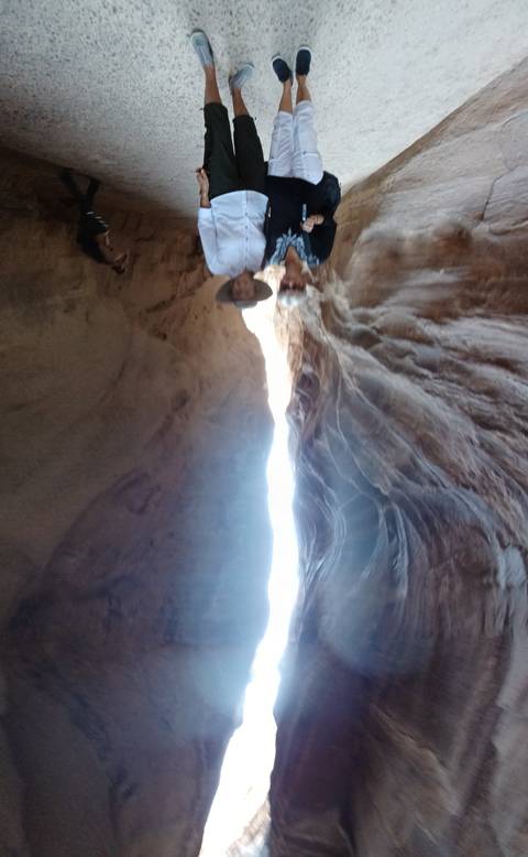 Two people walking through a narrow rock passage.